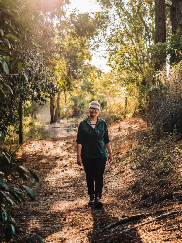 Individual walking through a forested area smiling at the camera.